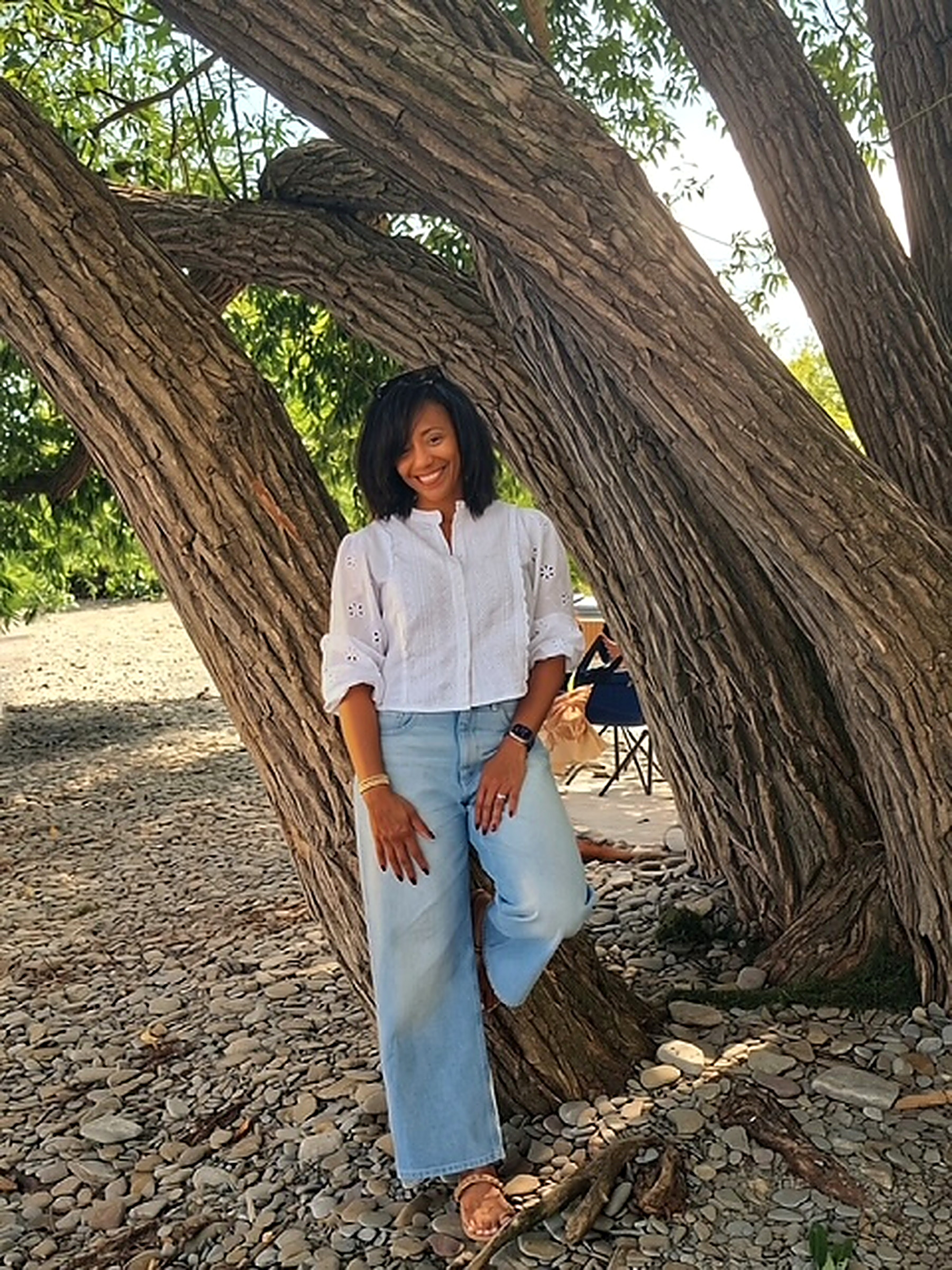 Francene Noel smiling under a large tree, wearing a white eyelet blouse and light jeans